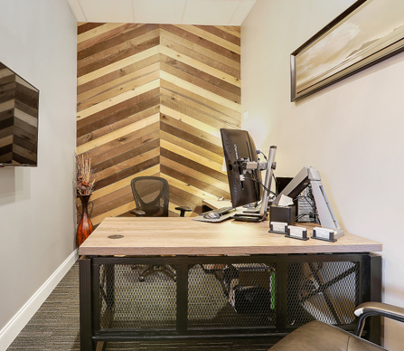 Modern dental office workspace with wooden desk, computer setup, and geometric wood wall accent.