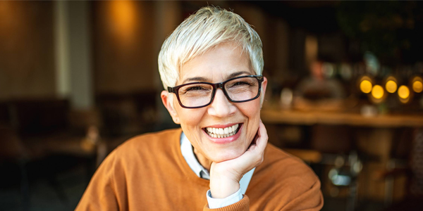 Smiling woman wearing glasses and orange sweater in dental office setting.