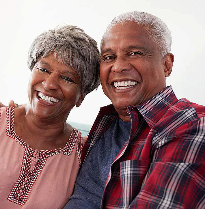 Two smiling seniors posing together against white background for dental practice portrait.