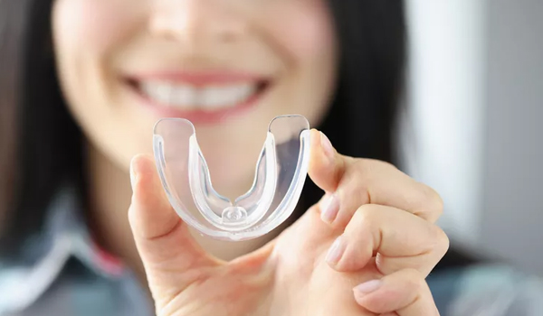 Smiling woman holding clear dental aligner tray in bright clinical setting.