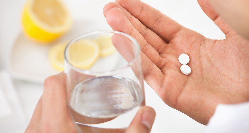 Hand holding aspirin tablets over glass of water, medication and healthcare concept.