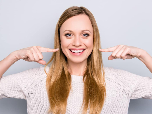 Smiling woman pointing to her teeth against white background for dental practice.
