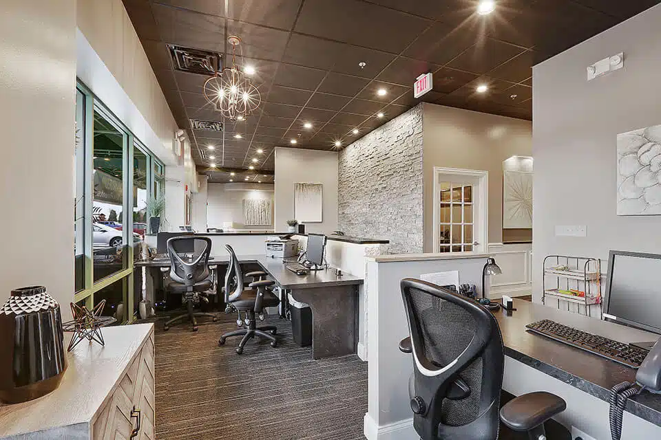 Modern dental office reception area with white desk, ergonomic chairs, and contemporary lighting fixtures.