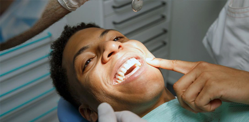 Man receiving dental treatment in dentist's chair with shaving cream applied to face.
